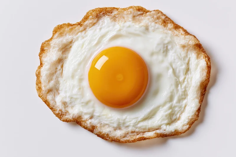 Single fried egg viewed from directly above on a plain white surface