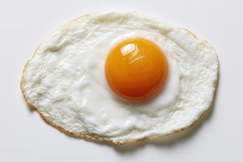 Single fried egg sunny side up resting flat on white surface