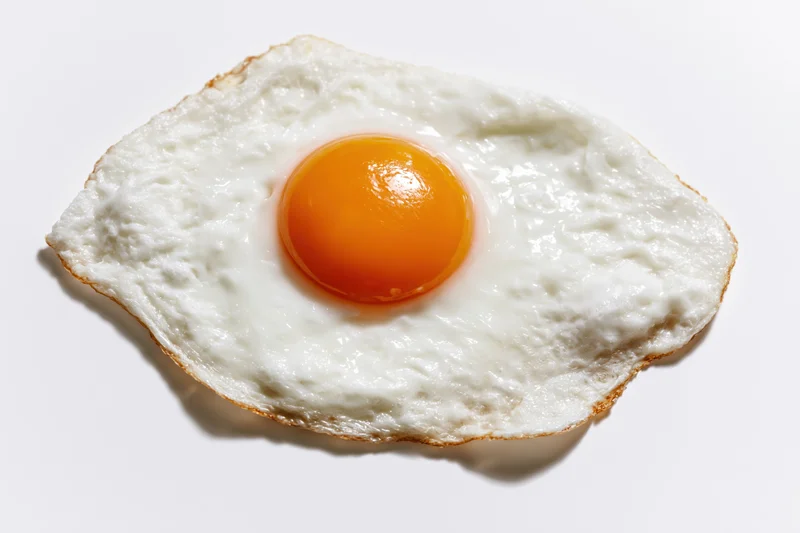 Single fried egg sunny side up resting flat on white surface