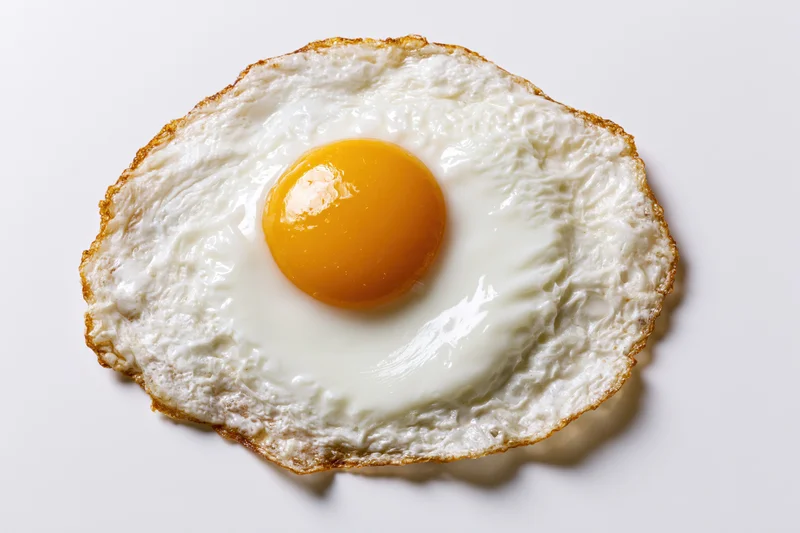 Single fried egg sunny side up on plain white surface