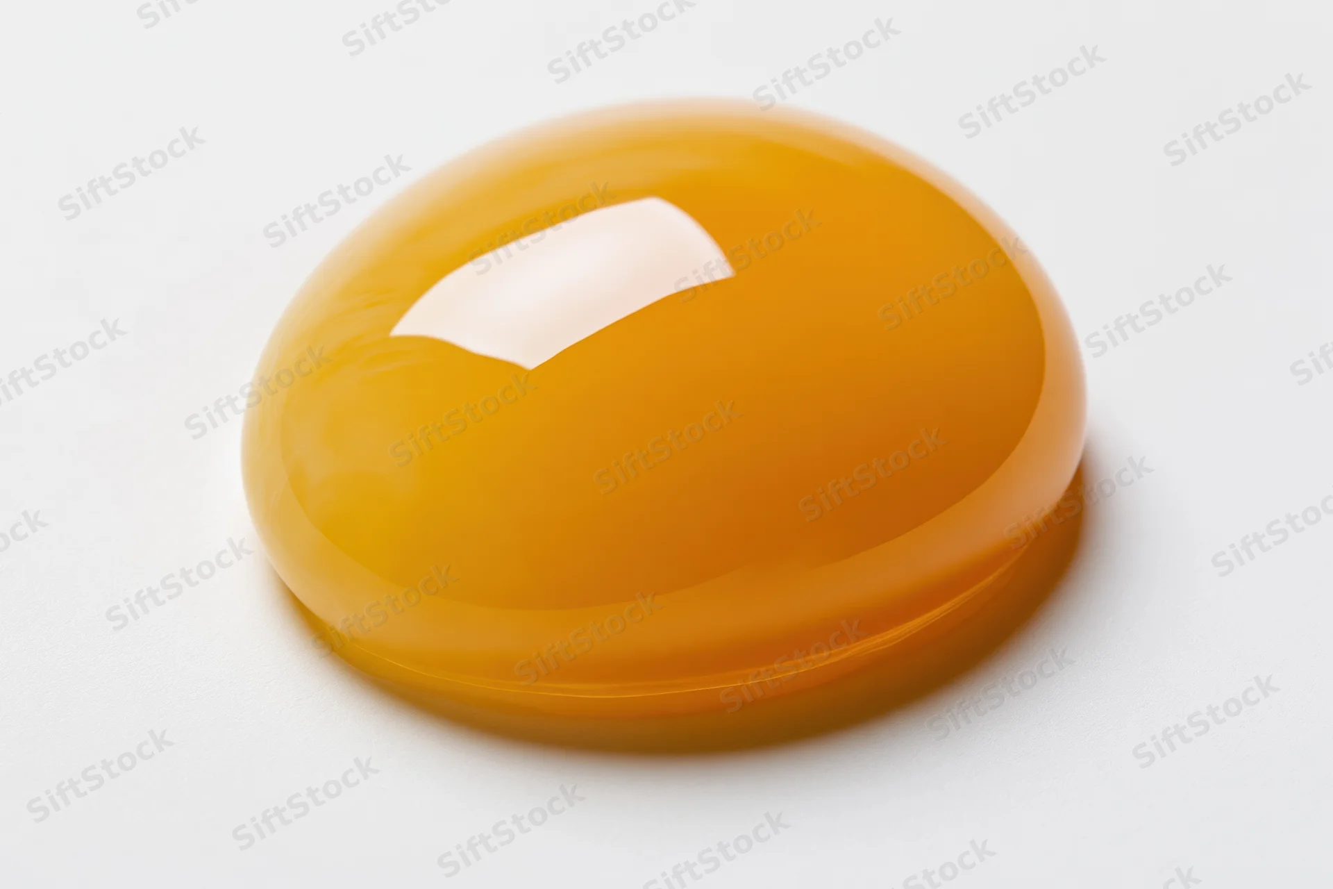 Raw egg yolk resting intact on a white surface