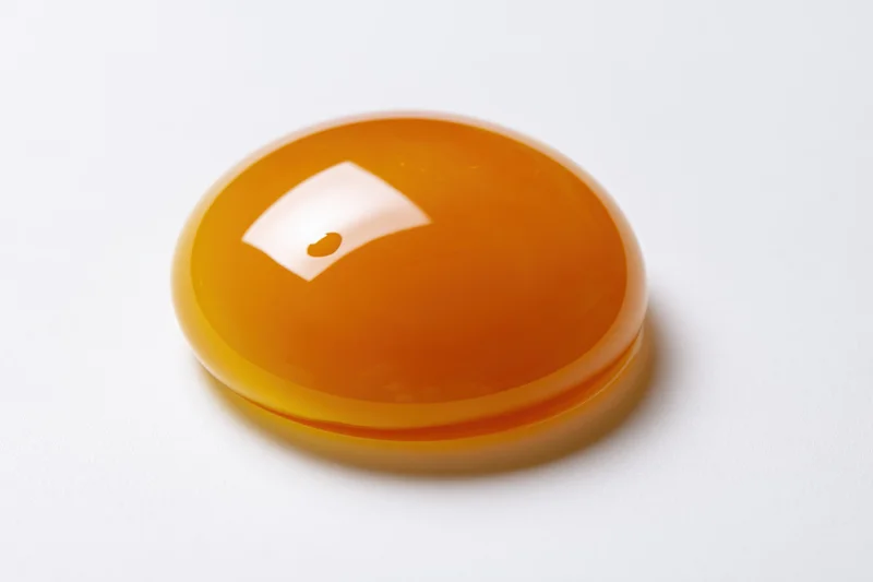 A single raw egg yolk resting intact on a plain white surface