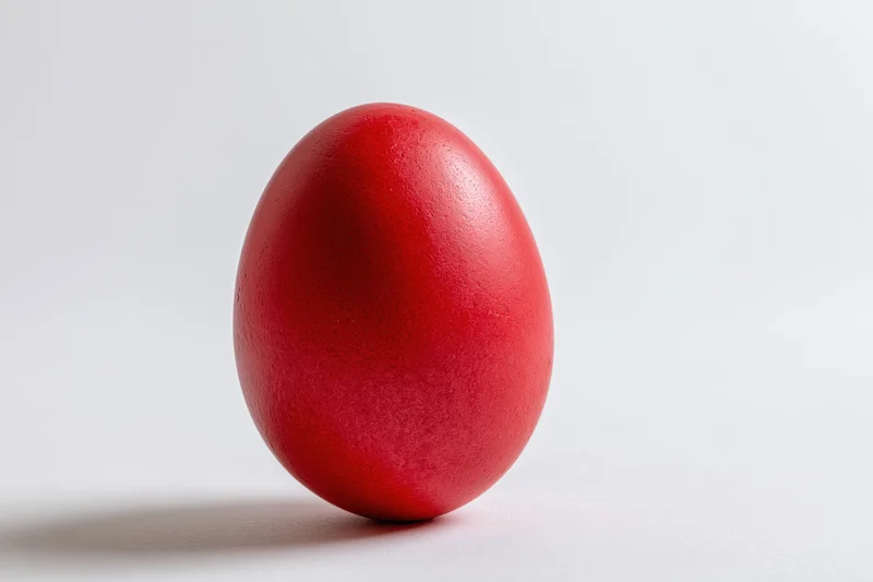 A single red-dyed easter egg standing upright on a plain white surface