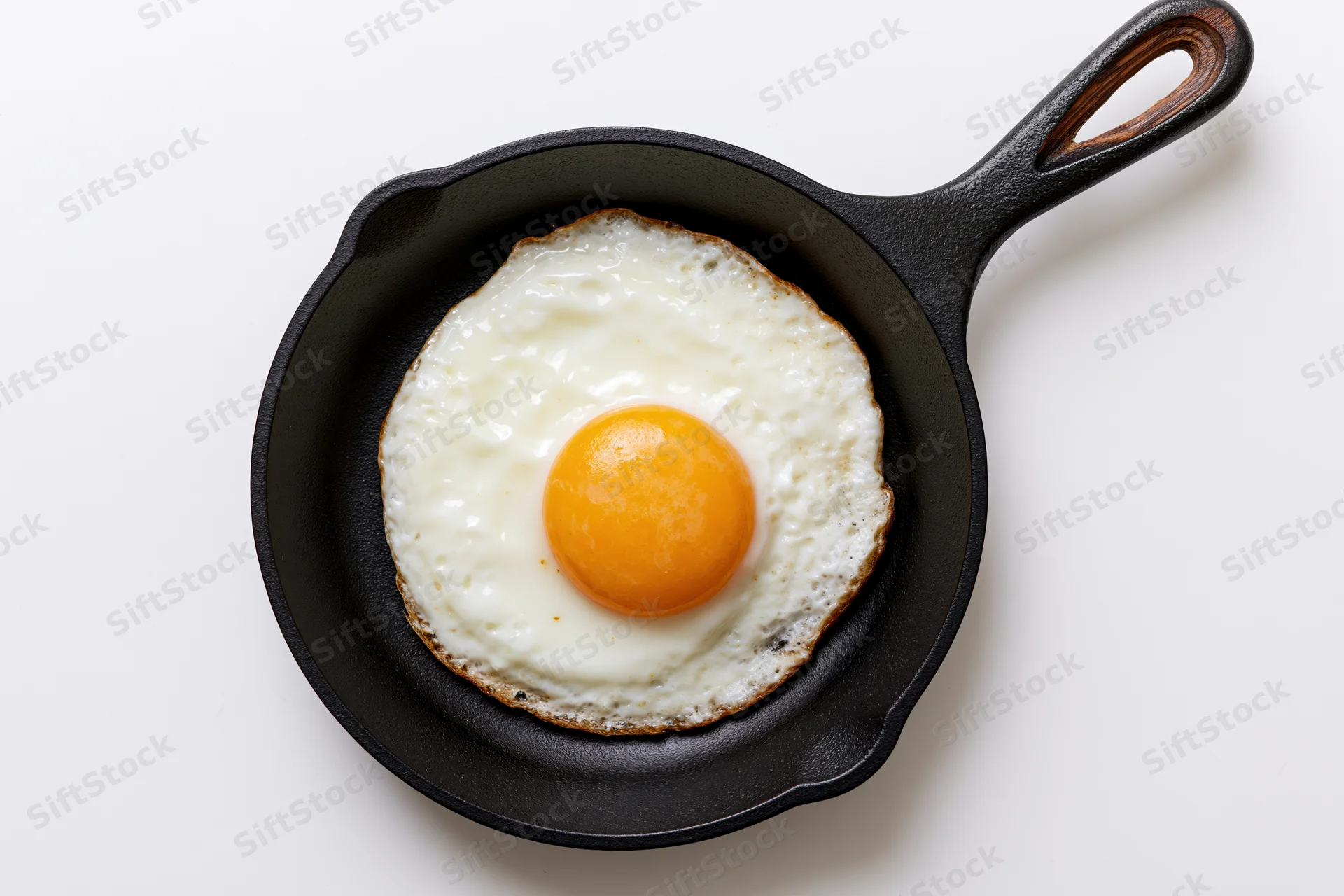 Sunny-side-up fried egg in a small black cast iron skillet on white background