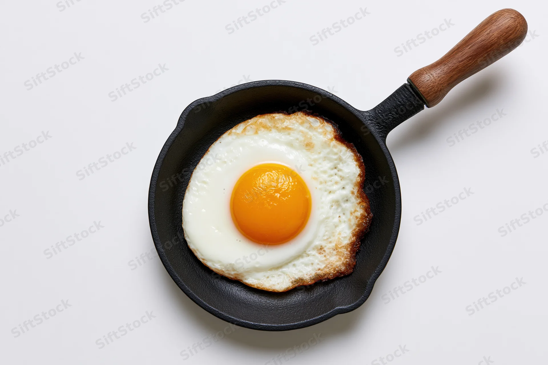 Sunny-side-up fried egg in a small black cast iron skillet with wooden handle on white background