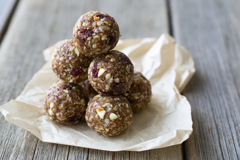 Homemade energy balls stacked in pyramid on crumpled parchment paper on wooden table