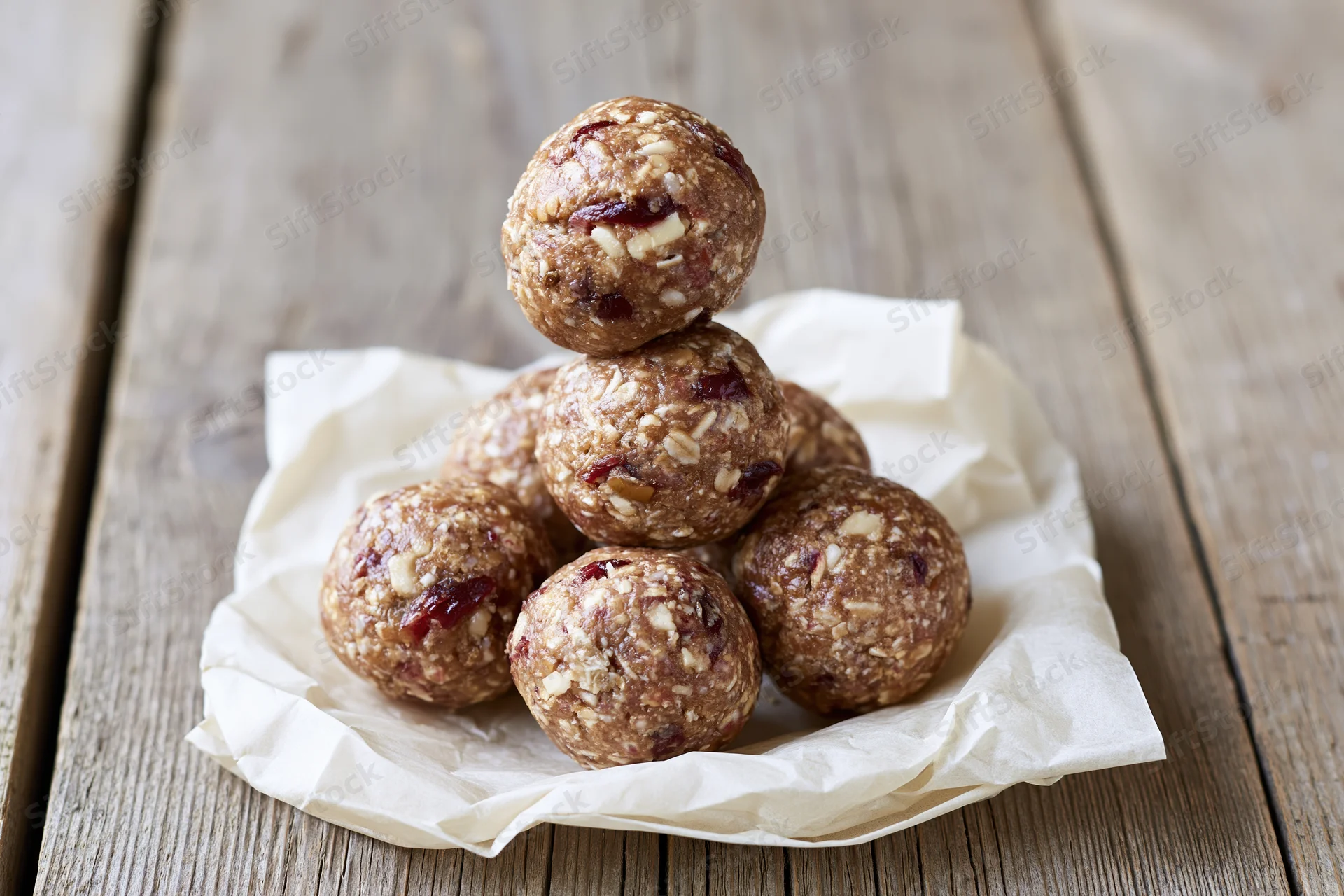 Homemade energy balls stacked in pyramid on parchment paper on wooden table