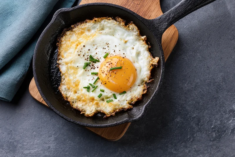 Sunny-side-up fried egg in a seasoned cast iron skillet on a wooden trivet