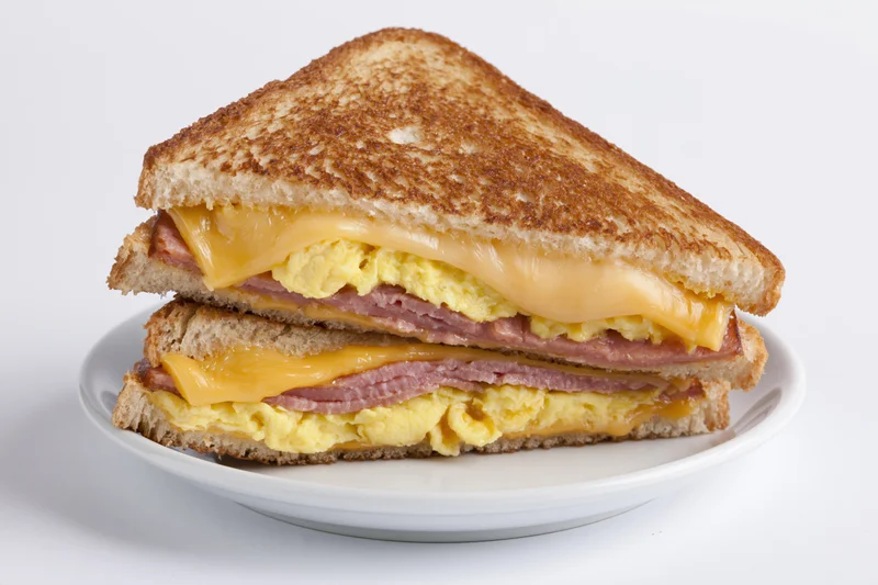 Grilled egg and cheese sandwich cut diagonally in half stacked on a white plate