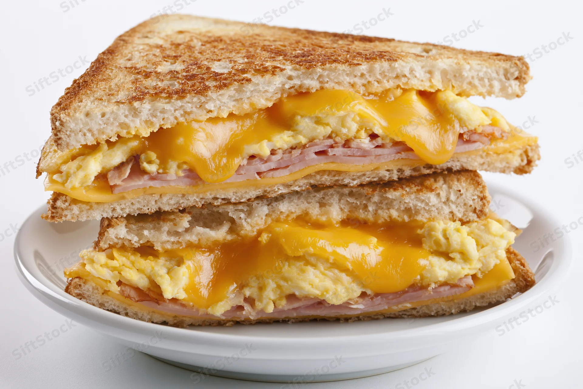 Grilled egg and cheese sandwich with ham cut diagonally and stacked on a white plate