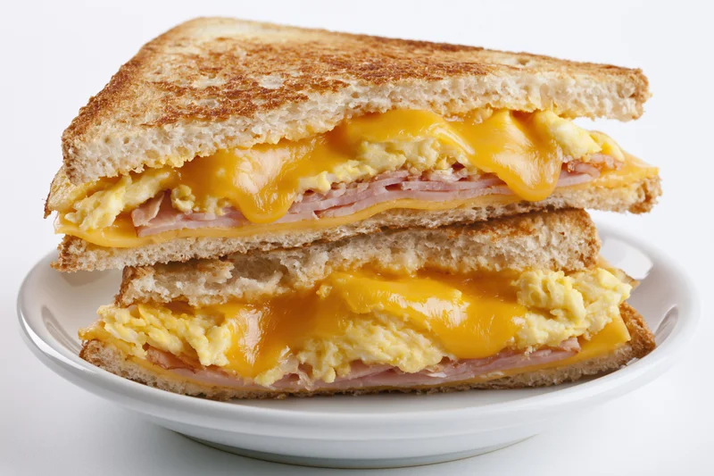 Grilled egg and cheese sandwich with ham cut diagonally and stacked on a white plate