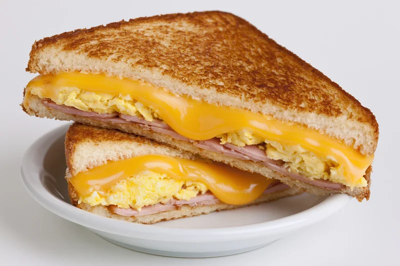 Grilled egg and cheese sandwich cut diagonally in half stacked on a white plate