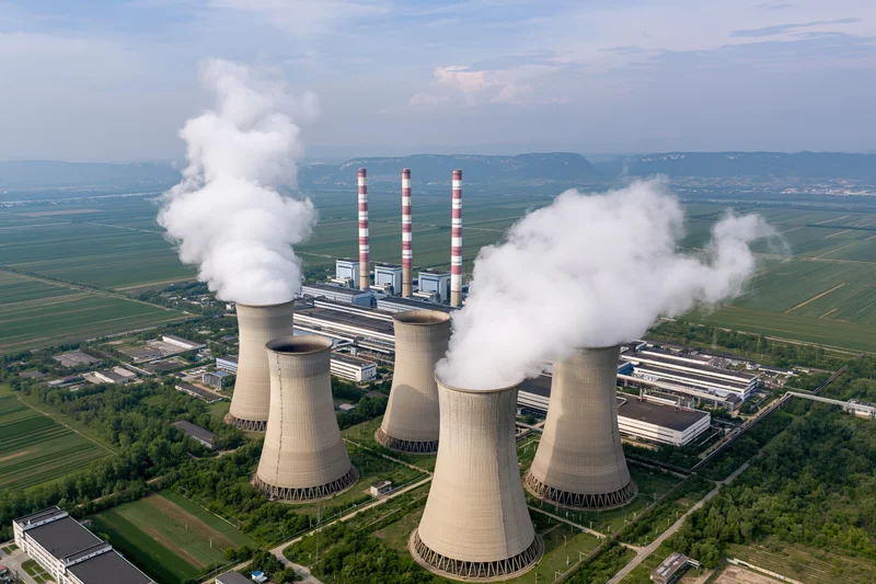 Aerial view of coal-fired powerplant with cooling towers emitting steam over rural farmland