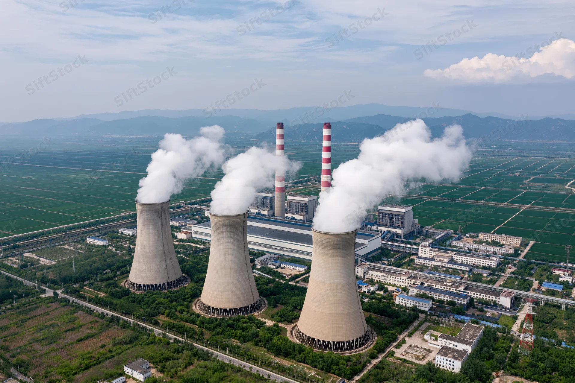 Aerial view of coal-fired powerplant with cooling towers emitting steam over farmland