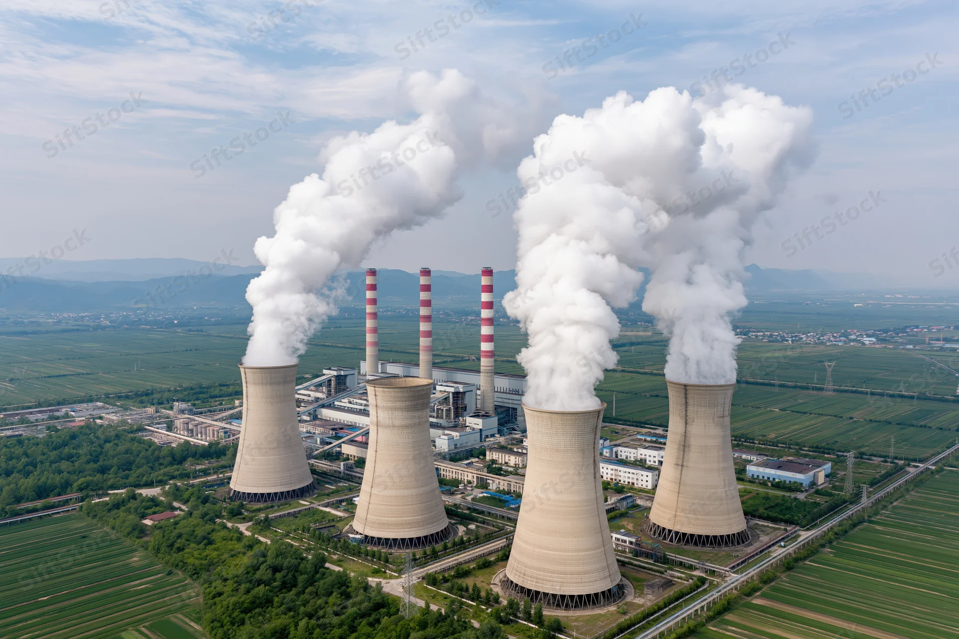 Aerial view of coal-fired powerplant with cooling towers emitting steam over green farmland