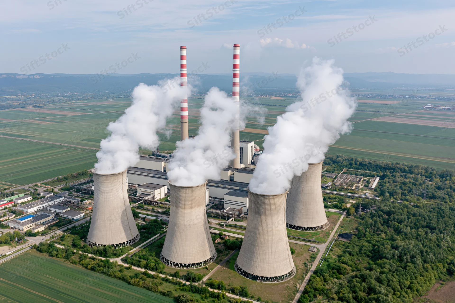 Aerial view of coal-fired powerplant with cooling towers emitting steam over rural fields