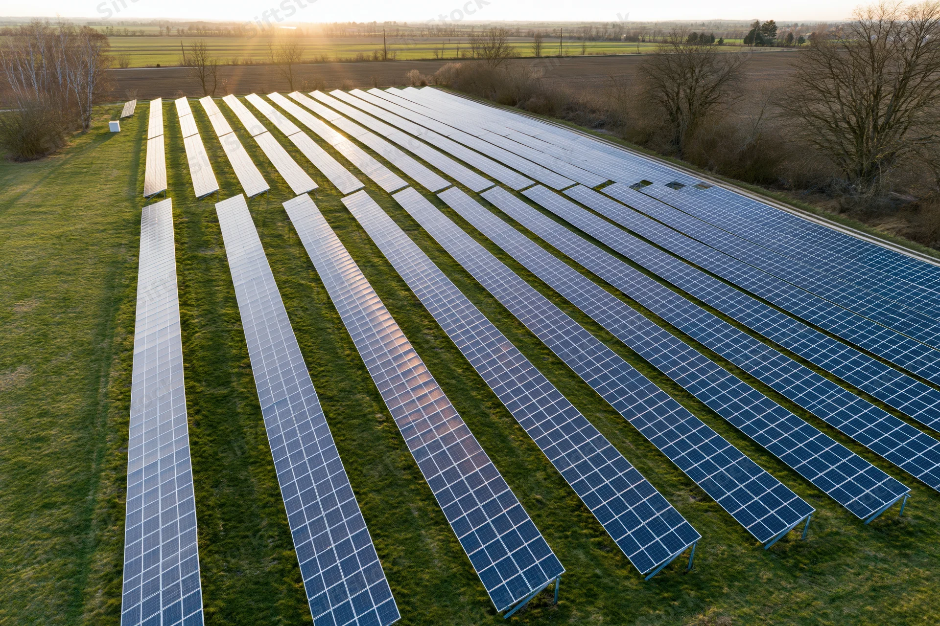 Rows of solar panels arranged in a field viewed from above during golden hour
