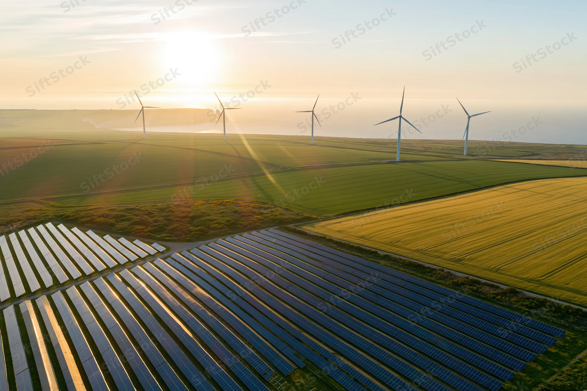 Aerial view of solar panels and wind turbines in a rural field at sunset