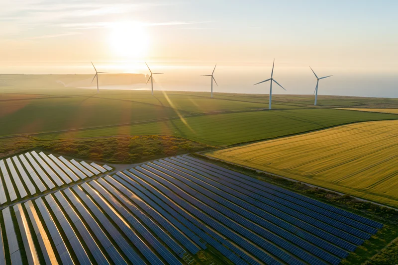 Aerial view of solar panels and wind turbines in a rural field at sunset