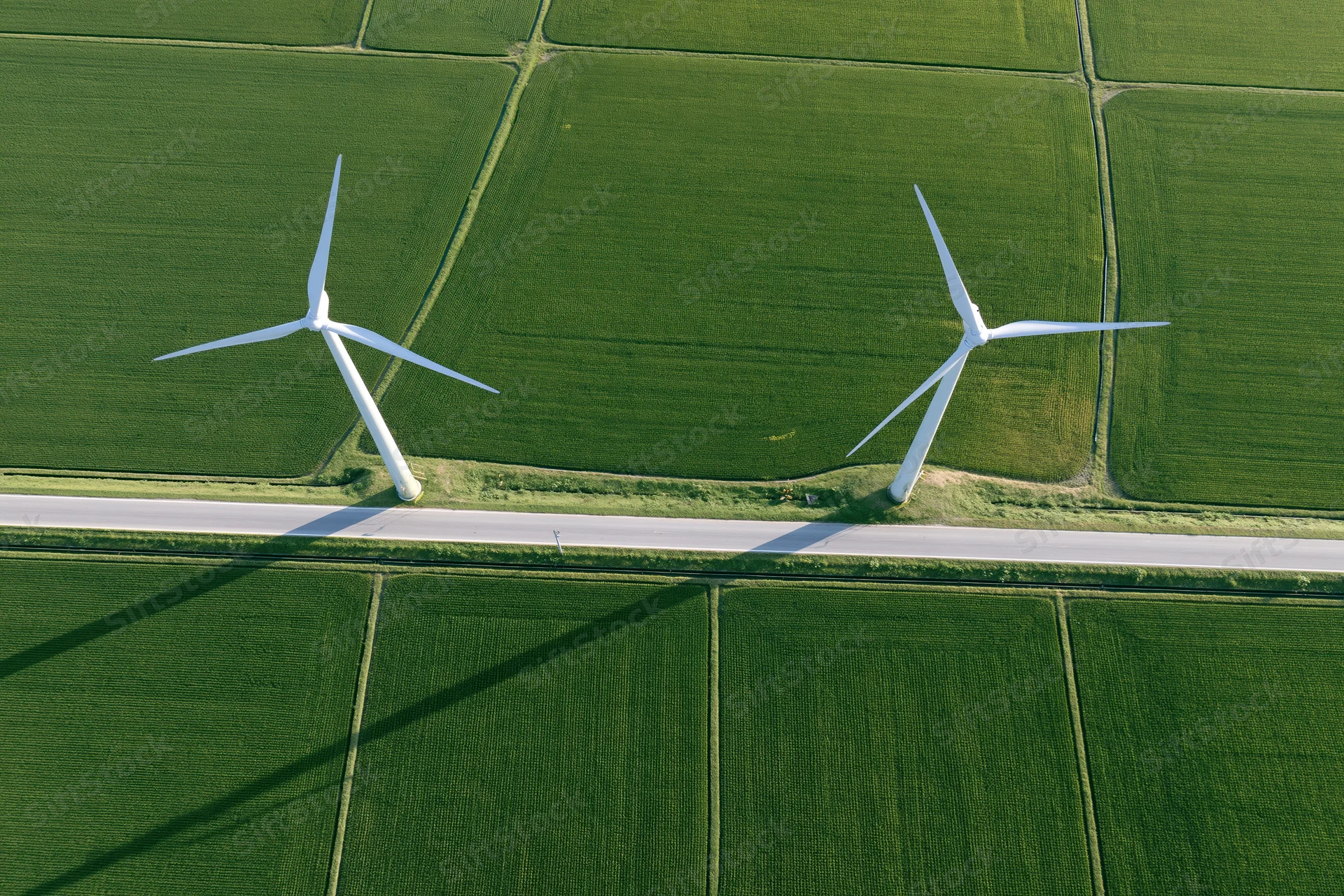 Two white wind turbines standing in a green agricultural field beside a road, viewed from directly above