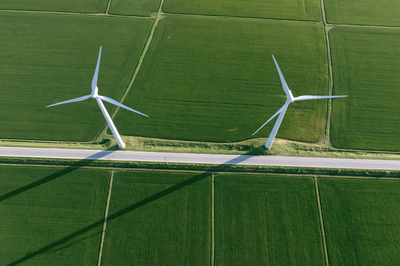 Two white wind turbines standing in a green agricultural field beside a road, viewed from directly above