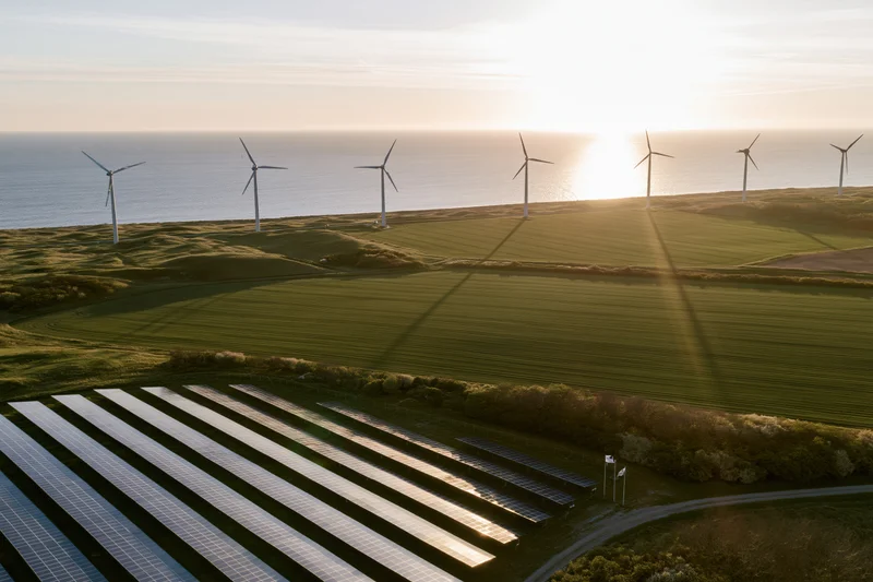 Rows of solar panels and wind turbines on a coastal field at sunset