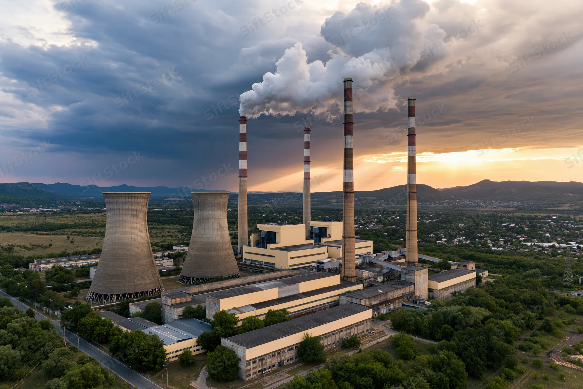 Aerial view of a coal-fired power plant with smokestacks emitting steam and smoke against a cloudy sunset sky