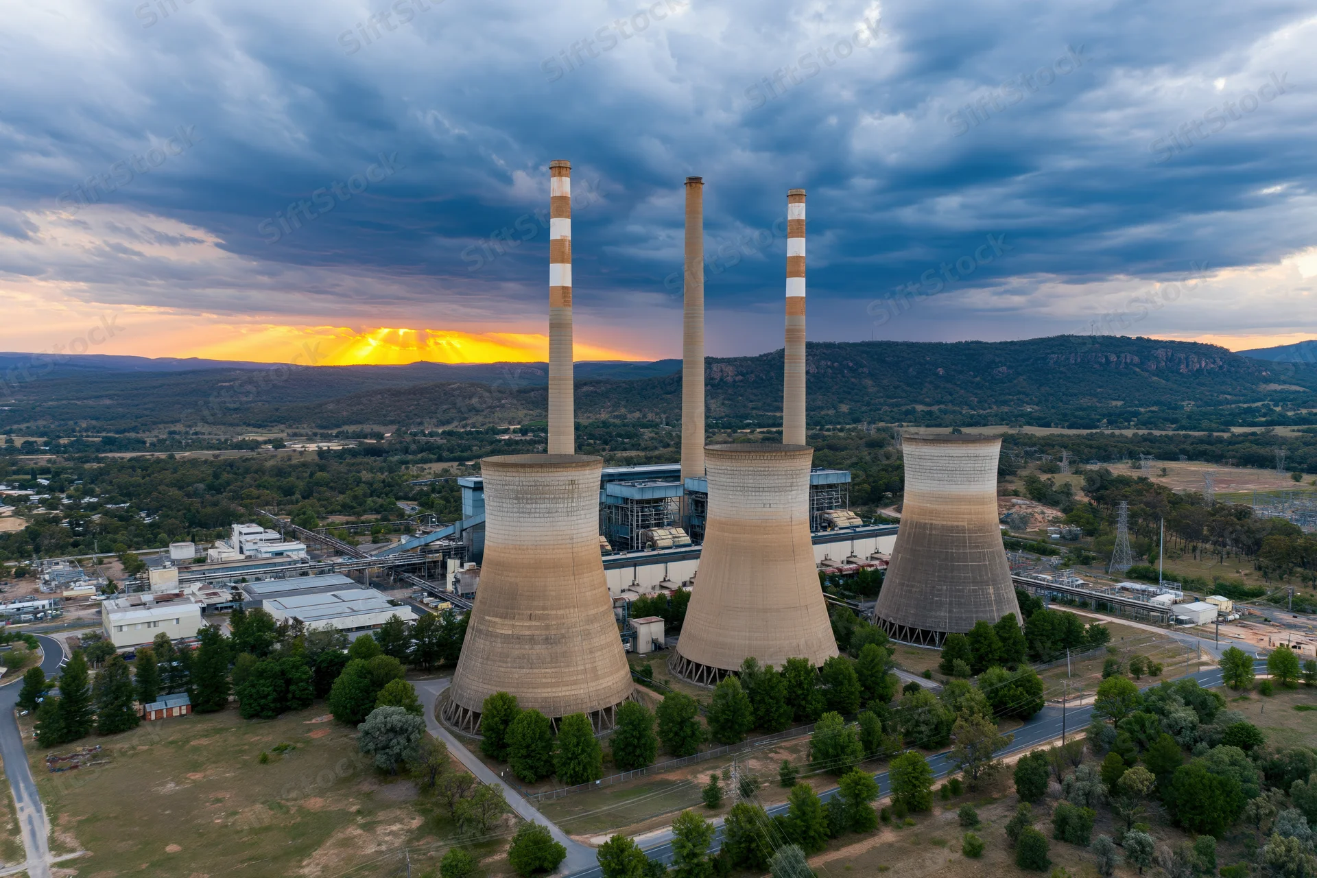 Aerial view of a coal thermal power plant with cooling towers and smokestacks at sunset near mountains