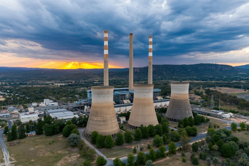 Aerial view of a coal thermal power plant with cooling towers and smokestacks at sunset near mountains