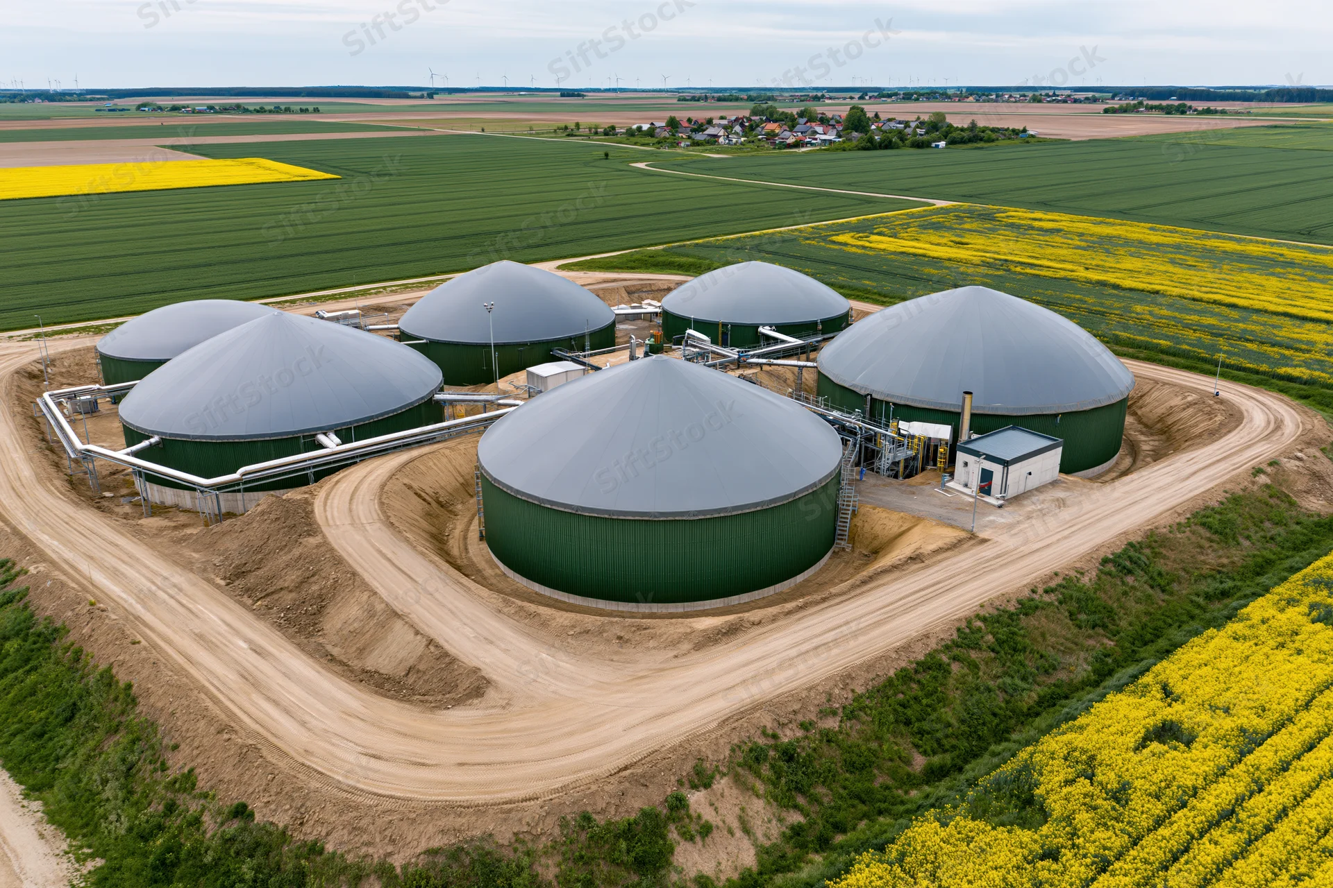 Aerial view of biogas plant with multiple domed digesters surrounded by rapeseed fields in rural countryside