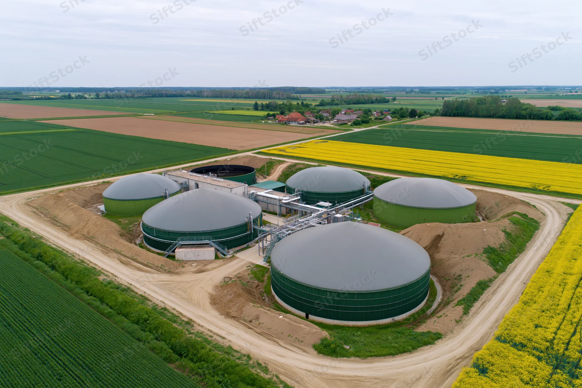 Aerial view of biogas plant with multiple digesters surrounded by farmland and rapeseed fields