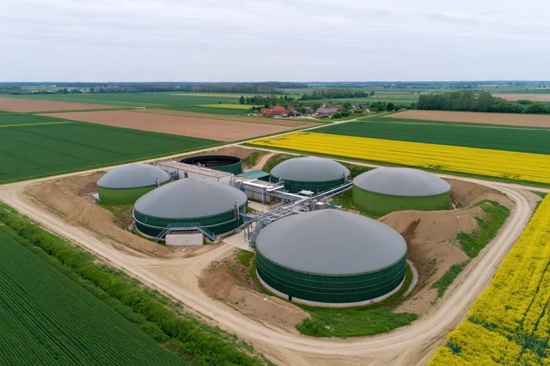 Aerial view of biogas plant with multiple digesters surrounded by farmland and rapeseed fields