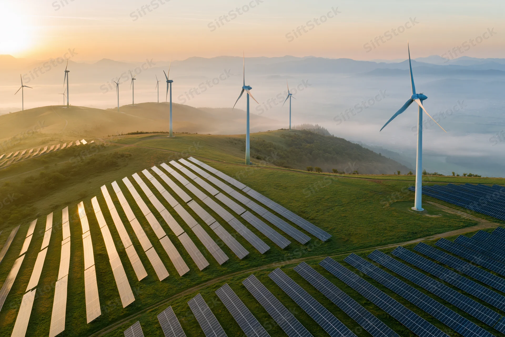 Aerial view of solar panels and wind turbines on rolling hills at sunrise