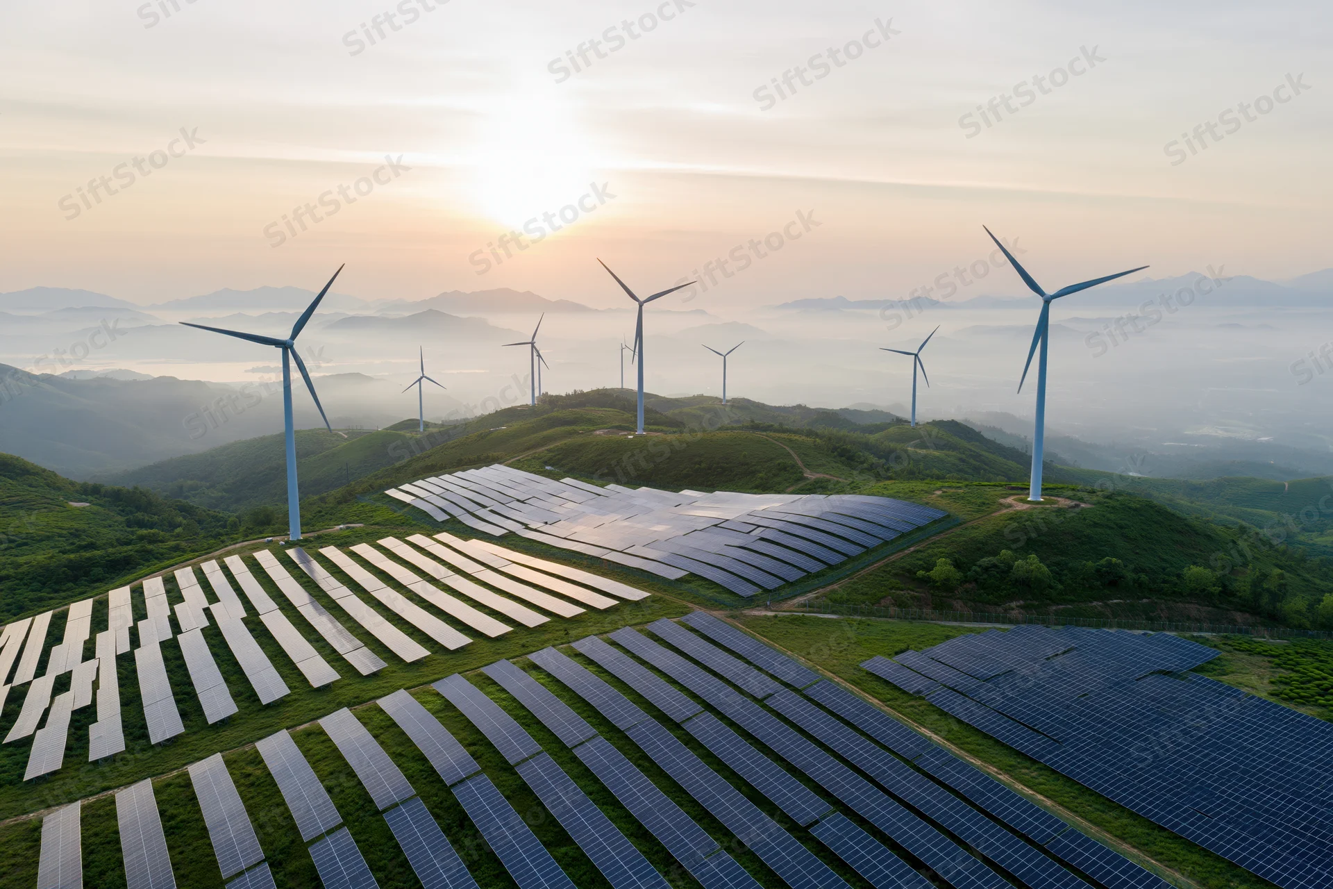 Aerial view of solar panels and wind turbines arranged on rolling green hills at sunrise