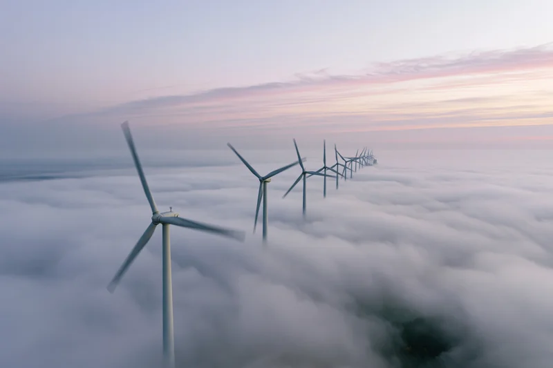 Row of wind turbines rising above a sea of clouds at twilight