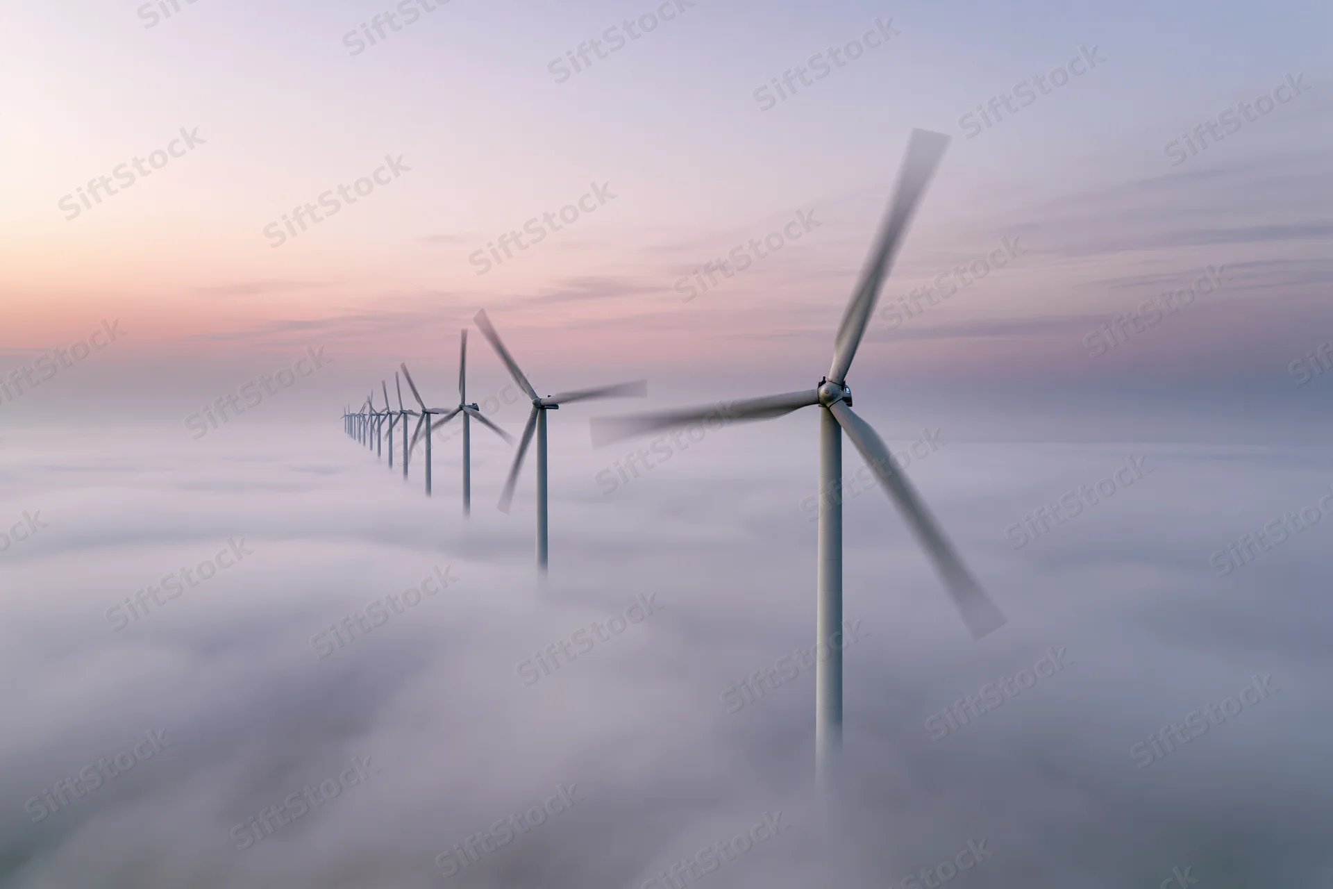 Row of wind turbines rising above a sea of fog at twilight