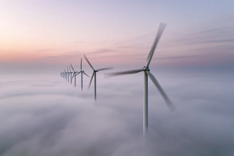 Row of wind turbines rising above a sea of fog at twilight