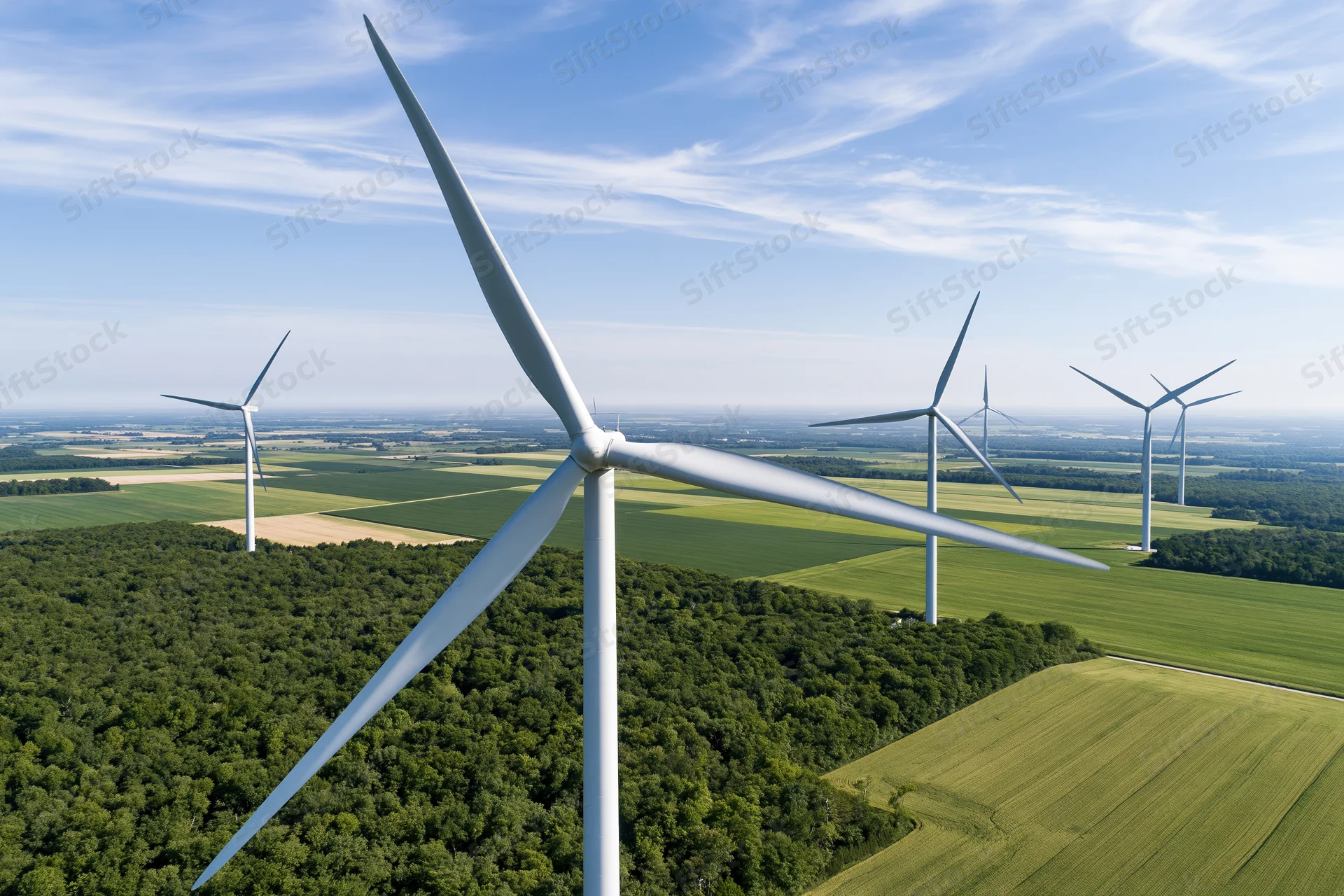 Aerial view of wind turbines in a rural landscape with fields and forest under a blue sky