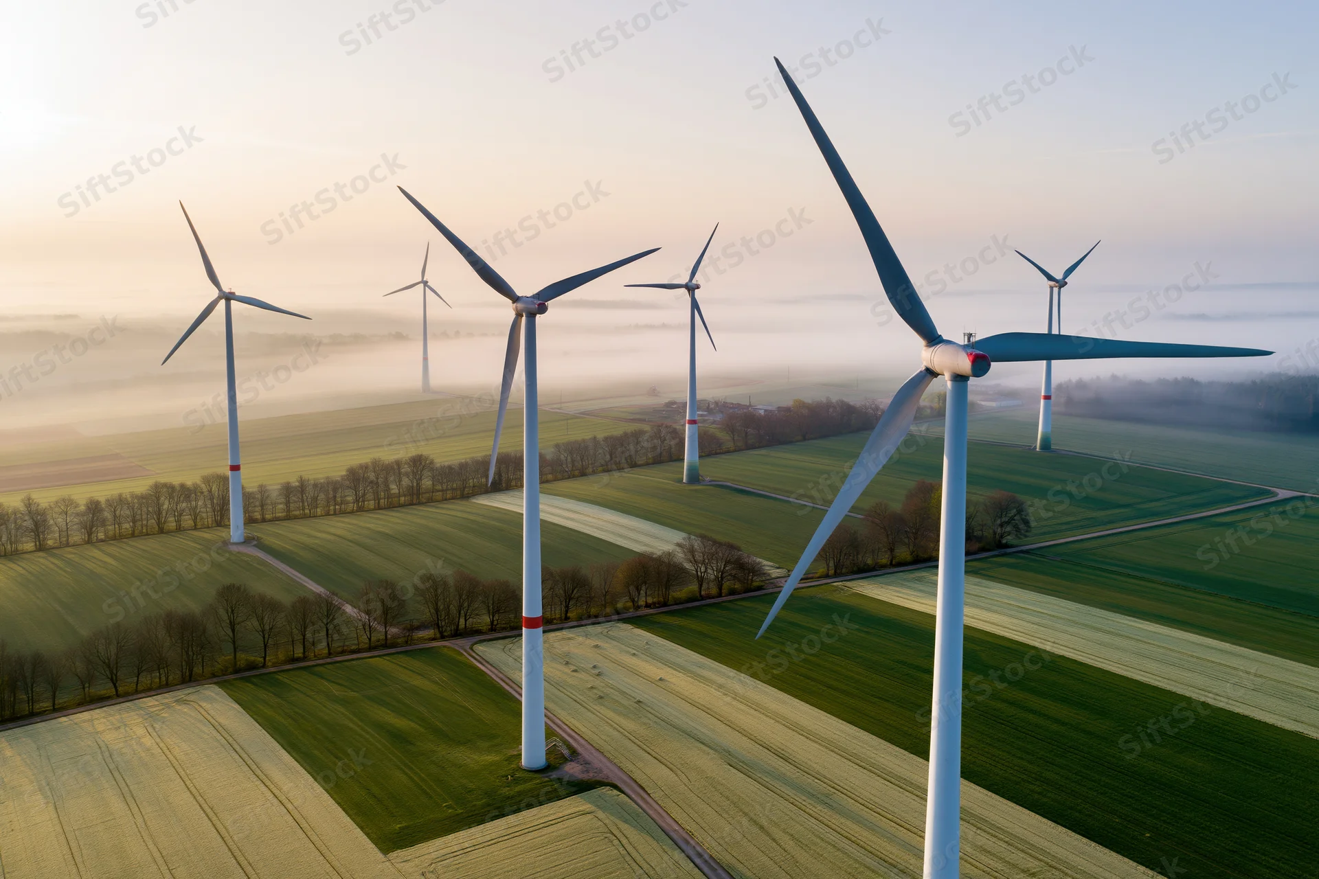 Wind turbines standing in a green agricultural field under a misty morning sky, viewed from above