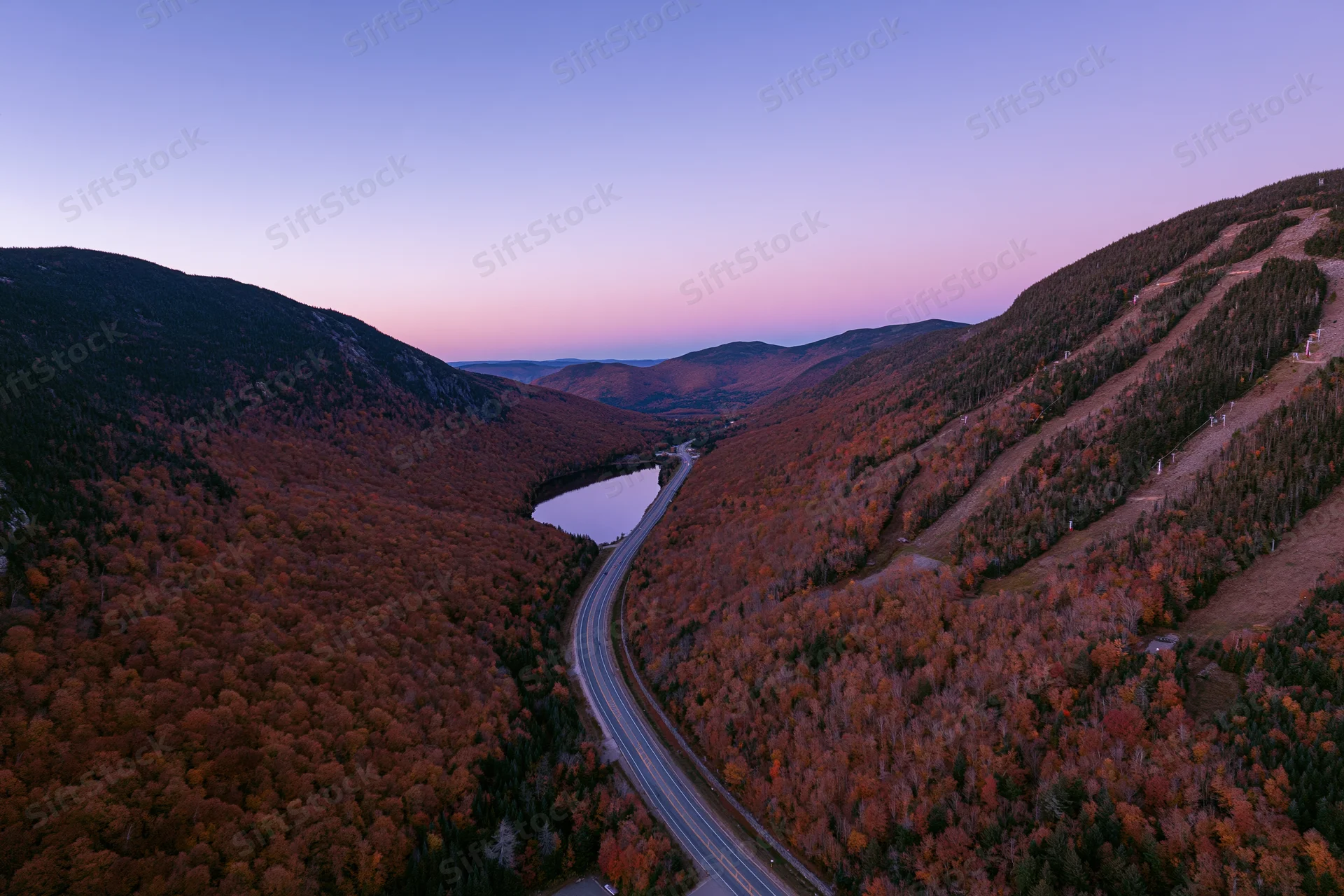 Aerial view of a winding highway through a mountain valley in autumn foliage