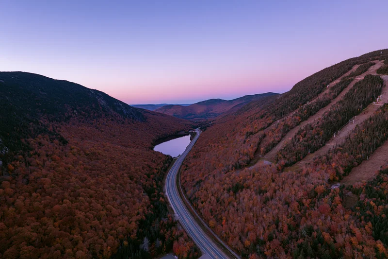 Aerial view of a winding highway through a mountain valley in autumn foliage