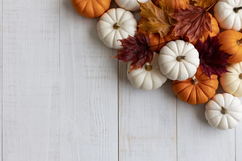 Small orange and white pumpkins with autumn maple leaves arranged on a white wooden table in a flat lay composition