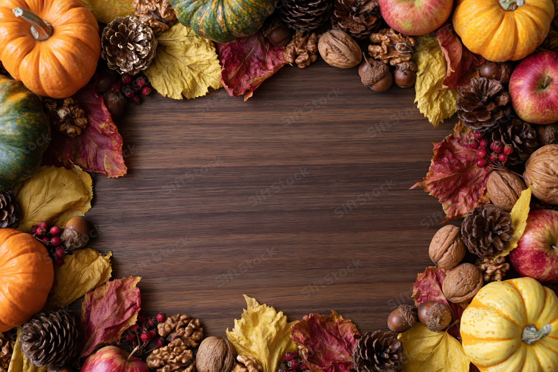 Autumn harvest flat lay arrangement framing the edges of a wooden table with pumpkins, apples, leaves, nuts and berries, leaving central copyspace