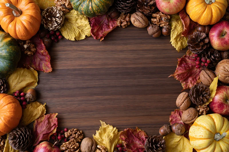 Autumn harvest flat lay arrangement framing the edges of a wooden table with pumpkins, apples, leaves, nuts and berries, leaving central copyspace