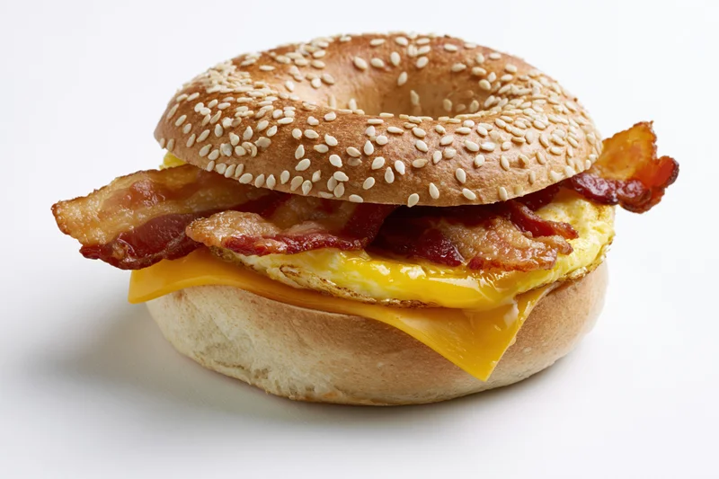 Bacon egg and cheese breakfast bagel sandwich on a plain white surface
