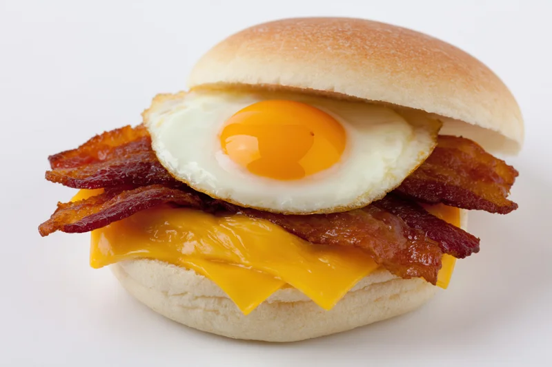 Bacon egg and cheese breakfast sandwich on a plain round bun with melted cheese and crispy bacon strips layered between the buns