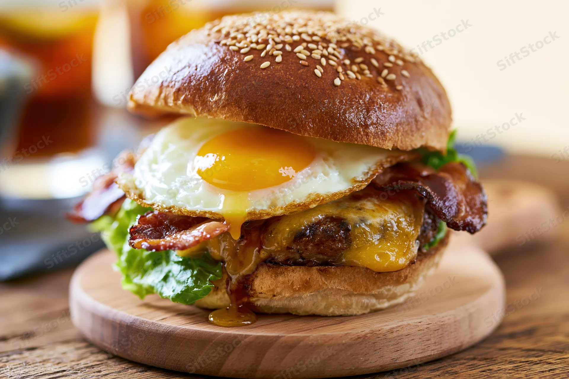 Breakfast burger with fried egg, crispy bacon, melted cheese, and lettuce on a sesame seed bun served on a wooden board