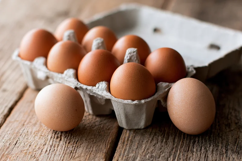 Brown chicken eggs in an open cardboard carton on a wooden table