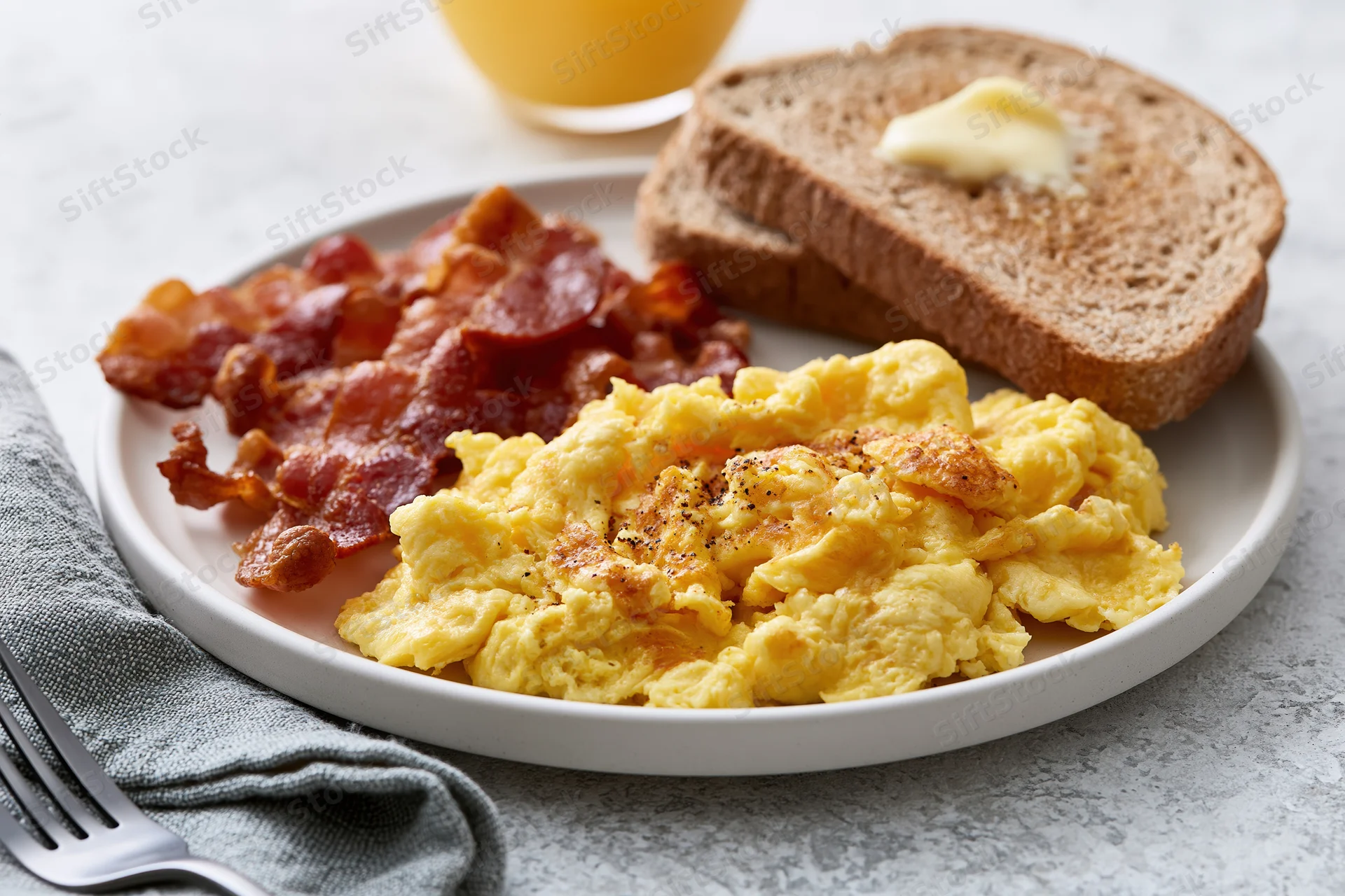 Classic american breakfast plate with scrambled eggs, bacon, toast and orange juice on a marble countertop