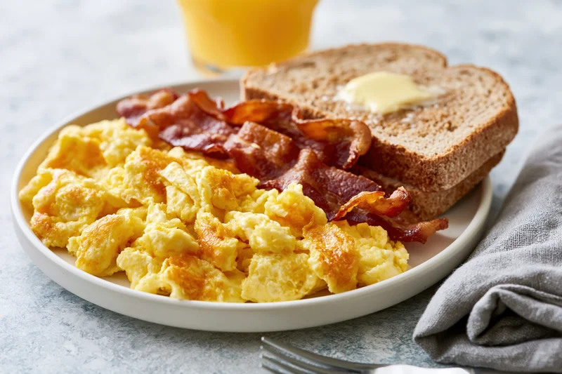 Classic american breakfast plate with scrambled eggs, bacon, toast and orange juice on a table